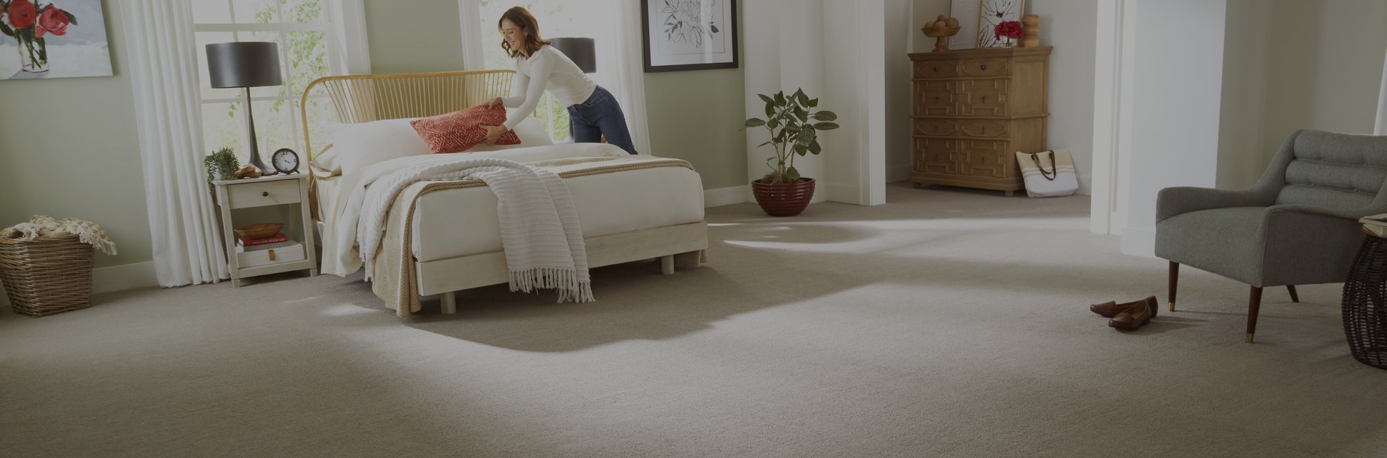 Woman making a bed in a bright open bedroom with carpet floors